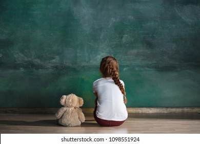 Little Autistic Girl With Teddy Bear Sitting On Floor At Empty Room. Autism Concept. Conceptual Image With Little Caucasian Model At Studio. Back View