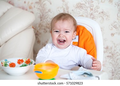 Little baby boy crying and screaming during eating, sitting in highchair