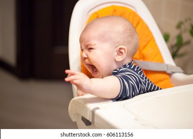 Little baby boy crying and screaming during eating, sitting in highchair