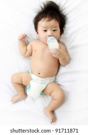 little baby boy drinks milk from bottle by him self, lying on bed