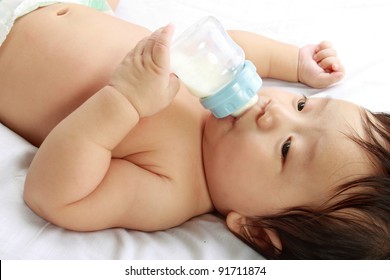 little baby boy drinks milk from bottle holded by him self, lying on bed