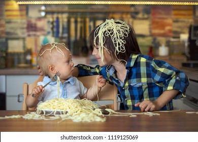 Little Baby Boy And His Older Brother, Toddler Child, Eating Spaghetti For Lunch And Making A Mess At Home In Kitchen