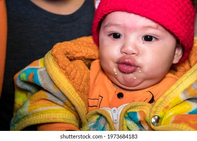 A Little Baby Boy Making A Weird Face While He Is Wearing Winter Clothes And Knitted Baby Hat.