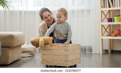 Little Baby Boy With Mother Collecting Toys In Wooden Toy Box At Living Room.