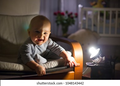 Little Baby Boy, Sitting In Rocking Chair, Looking With Curiousity At A Night Lamp, Dim Light