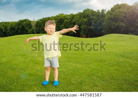 Little baby boy standing on the green grass. Summer walk. Hands to the side. Greeting and singing. Joy hand gestures. Empty t-short  template no print you can place image brand logo or ad information