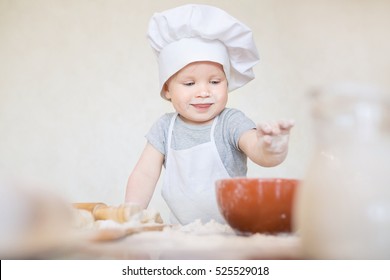 The little baby boy in a suit of the cook sculpts dough. Small kid scullion make dinner in chef suit. Cooking child lifestyle concept. Toddler enjoy, having fun, learning and playing in the kitchen