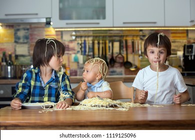 Little Baby Boy, Toddler Child And His Older Brothers, Eating Spaghetti For Lunch And Making A Mess At Home In Kitchen