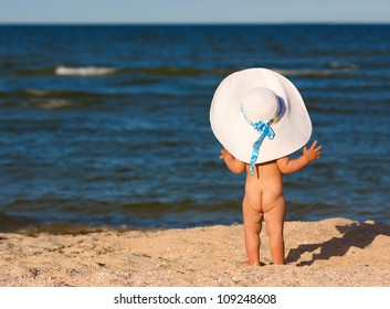 Little Baby Girl In Big Hat On The Beach Looking At Sea