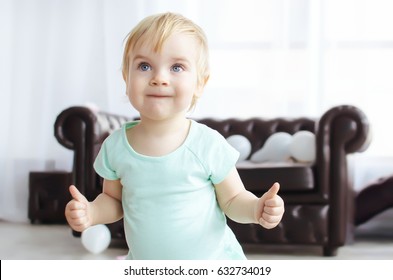 Little baby girl in blue dress shows thumbs up on both hands