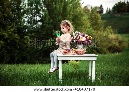 Little baby girl eating chocolate cake and drinking a beverage outdoors at the picnic. The concept of a happy childhood