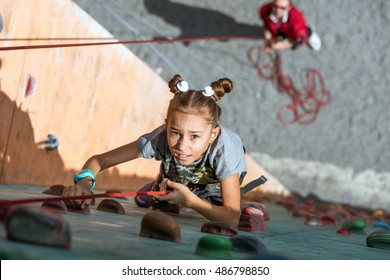 Little baby girl with funny hear style climbing vertical wall and man belaying her from below - Powered by Shutterstock