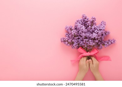 Little baby girl hands holding fresh beautiful flower bouquet of purple lilac with ribbon on light pink table background. Pastel color. Closeup. Point of view shot. Empty place for text. - Powered by Shutterstock