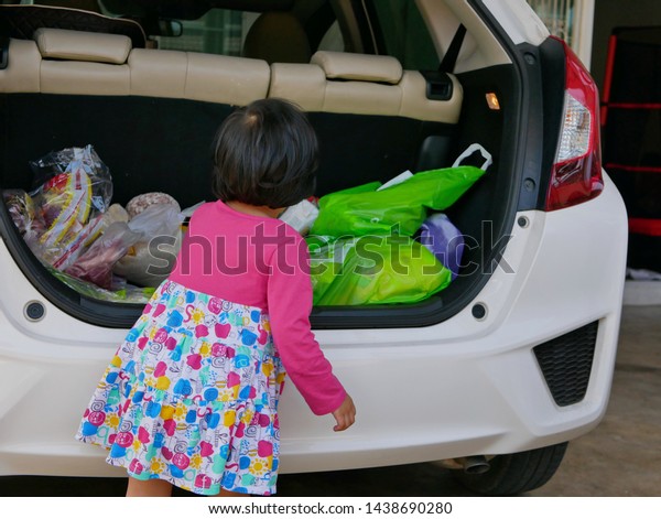 Little baby girl help carrying stuff from the back
of the car into the house, after coming back from shopping at a
supermarket - children's development by allowing them to help doing
everyday tasks 