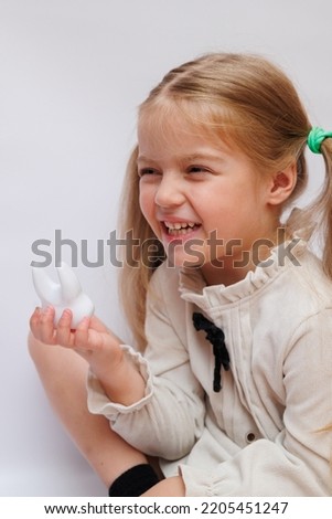 Little baby girl hold big toy artificial plastic tooth. Closeup of toy tooth in child's hands. Girl make funny face. Conception of safe stomatological treatment for children. White background.