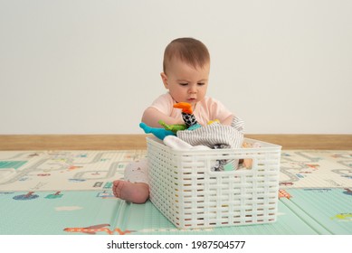 Little Baby Girl Looking For A Toy Into A White Toy Box With A Concentrated Gesture. Baby Playing At Home.