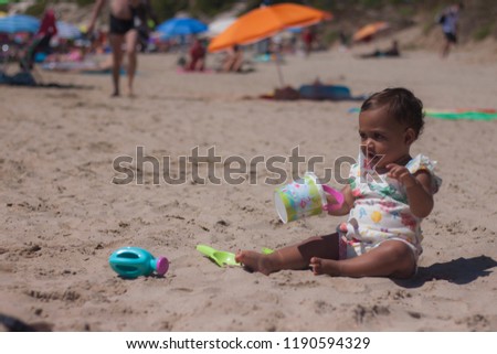 Little baby girl on the beach in a little dress playing with her toys in the sand