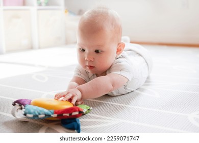 Little baby girl is playing with a toy during tummy time. Baby reaching for a musical toy. Baby development