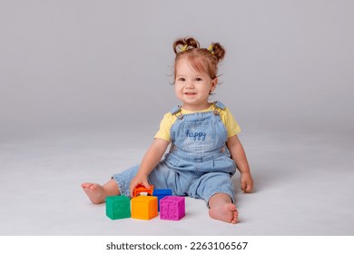 little baby girl is sitting on a white background and playing with colorful cubes. kid's play toy cubes