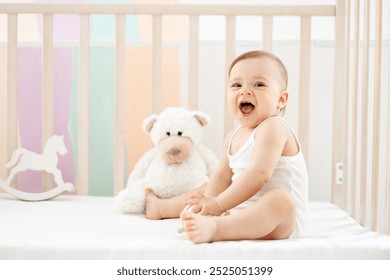 little baby girl smiling or laughing in the crib at home in the nursery in a white bodysuit, cute funny baby playing with soft and wooden toys before going to bed, lifestyle - Powered by Shutterstock