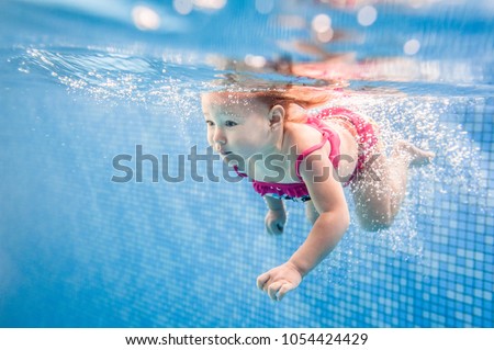 Little baby, girl swimming under water in paddling pool. Diving baby. Learning infant child to swim. Enjoy of swimming and bubbles.