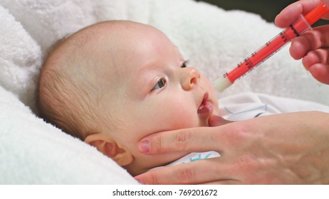 Little baby girl is taking juice medicine helping by a syringe handled by mother