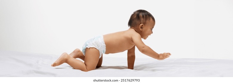 Little baby girl toddler in diaper crawling cheerfully on bed isolated on white studio background. Exploring and playing. Education. Concept of childhood, parenthood, care. Banner. Copy space for ad