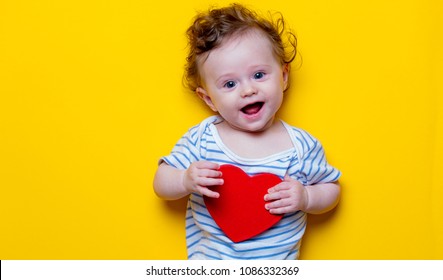 Little Baby With Heart Shape Toy On Yellow Background