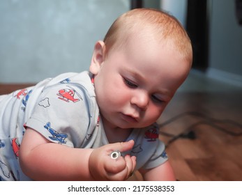 A little baby is holding a dangerous battery in his hands. The boy takes a life threatening small object in his mouth - Shutterstock ID 2175538353