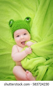 Little Baby In Knitted Frog Hat On Soft Blanket On Green Background