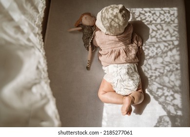 Little Baby Laying On Tummy With Her Doll, Side Beautiful Sun Light Through Window.