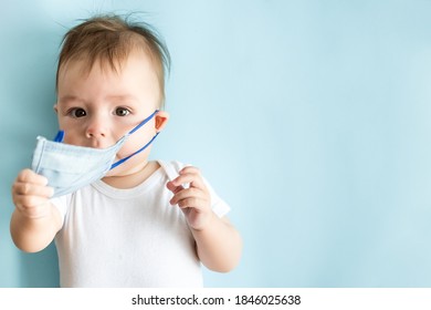 Little baby in medical mask on blue background. Concept covid-19 coronavirus pandemic. Child does not want to wear face mask and takes off it. Top view. Copy space.