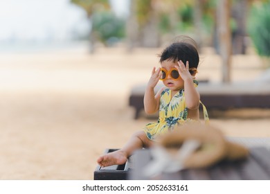 Little baby with orange sunglasses sitting on a beach chair
