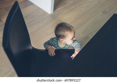 A Little Baby Is Using A Chair To Pull Himself Up