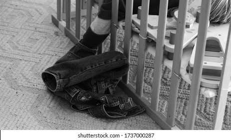 Little Baby In A Wooden Cot, Reaching Trousers Outside Of It.