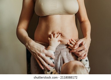 Little baby's hands on woman's belly full of stretch marks after pregnancy. Close up view.