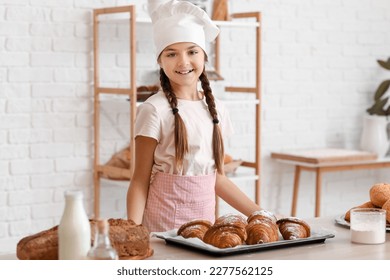 Little baker and tray with tasty croissants on table in kitchen