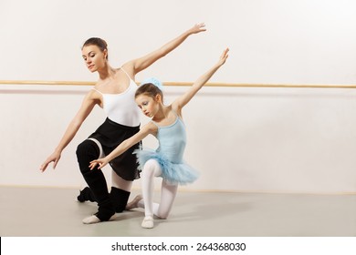 Little ballerina dancing with ballet teacher in dance studio. They both wearing a white tutu and leotard