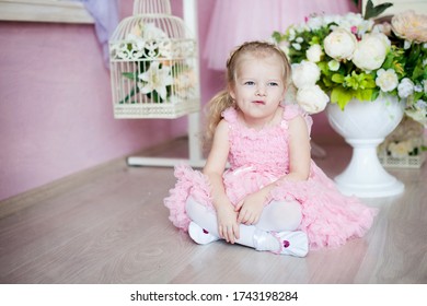 A Little Ballerina In A Dress Sits In A Dance Class On The Floor. Legs Crossed, Mischievous Face.