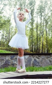 a little ballerina girl shows elements of choreography on a summer day on a path in the park - Shutterstock ID 2214227277
