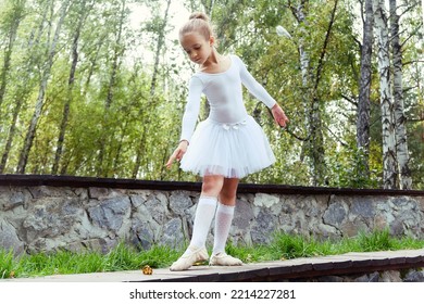 a little ballerina girl shows elements of choreography on a summer day on a path in the park - Shutterstock ID 2214227281