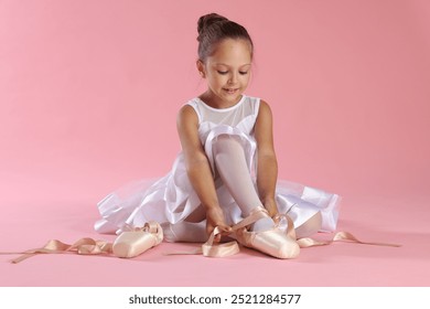 Little ballerina tying pointe shoes on pink background - Powered by Shutterstock