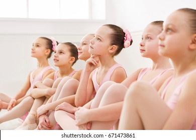 Little ballerinas in ballet studio. Group of girls having break in practice, sitting on floor. Classical dance school
