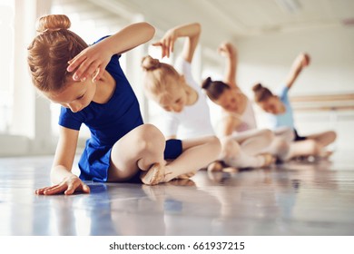 Little ballerinas doing exercises and bending sitting on floor in ballet class.