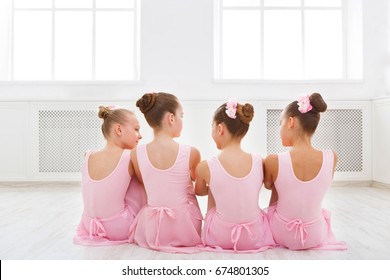 Little ballerinas talking in ballet studio. Group of girls having break in practice, sitting on floor, back view. Classical dance school
