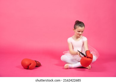 Little Ballet Dancer Kid Wearing Boxing Gloves While Sitting On Floor. Kid Isolated On Vibrant Pink Background. Female Stereotypes Concept.