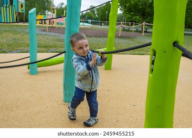 A little barefoot boy in denim clothes is walking on a modern wooden playground - Powered by Shutterstock