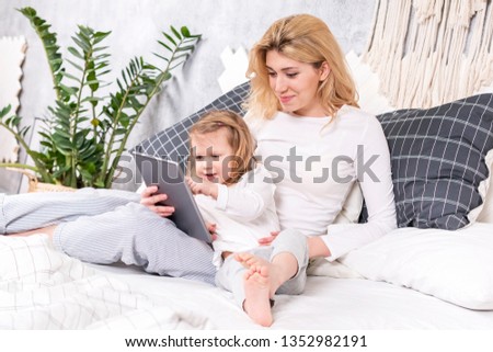 little beautiful daughter shows her mother finger on the tablet, sitting on the bed