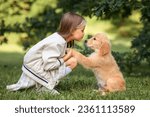 a little beautiful girl in a beige jacket and a plaid skirt with small golden retriever puppies dogs plays in the park in summer