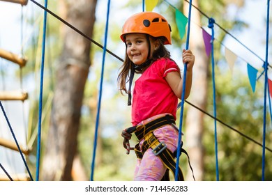 Little beautiful girl climbs on rope harness in summer city park. - Powered by Shutterstock